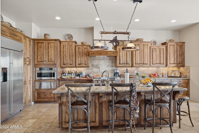 kitchen featuring stainless steel appliances, a kitchen breakfast bar, light stone counters, decorative backsplash, and a center island with sink