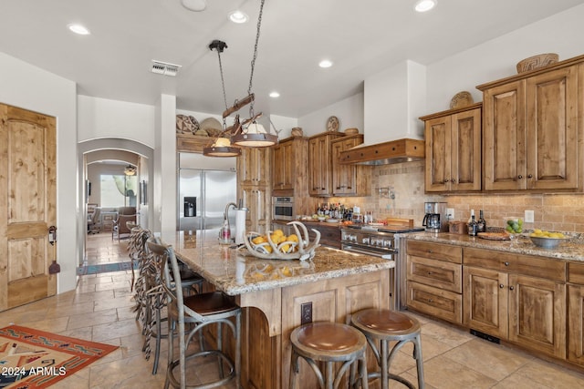 kitchen with high quality appliances, a center island with sink, light stone counters, and custom exhaust hood