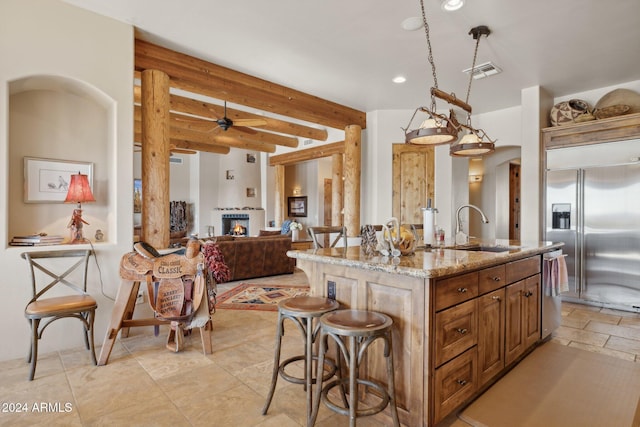 kitchen featuring light stone countertops, sink, ceiling fan, stainless steel appliances, and an island with sink