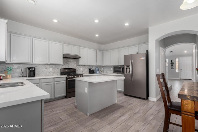 kitchen with stainless steel appliances, light countertops, a kitchen island, a sink, and under cabinet range hood