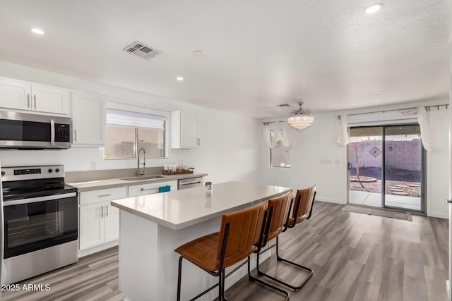 kitchen with sink, a breakfast bar, appliances with stainless steel finishes, white cabinetry, and a kitchen island