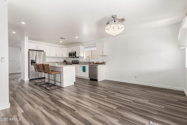 kitchen with appliances with stainless steel finishes, white cabinets, dark hardwood / wood-style flooring, a kitchen bar, and a center island