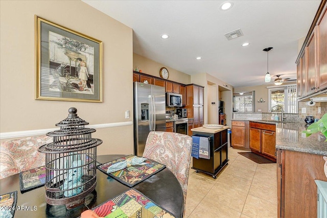 kitchen with sink, hanging light fixtures, light stone countertops, appliances with stainless steel finishes, and kitchen peninsula