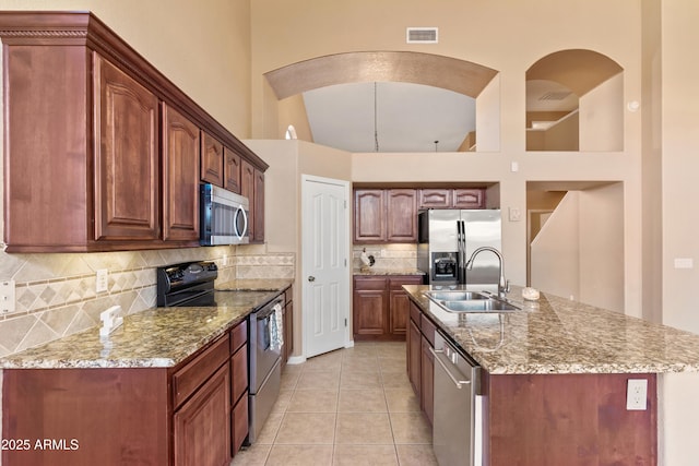 kitchen with a high ceiling, backsplash, stainless steel appliances, and an island with sink