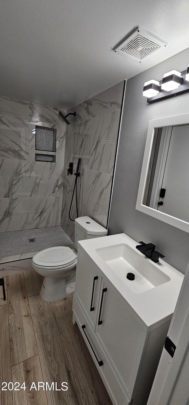 bathroom with a textured ceiling, a tile shower, wood-type flooring, vanity, and toilet