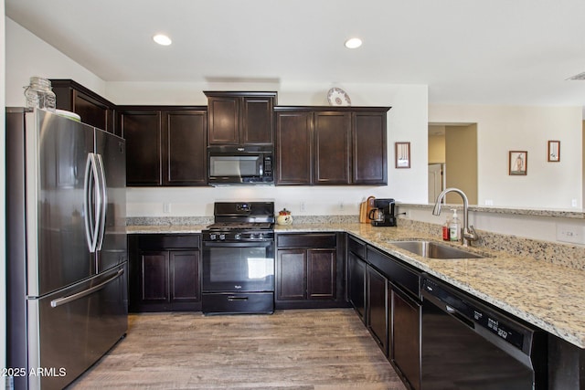 kitchen with sink, light hardwood / wood-style flooring, light stone counters, black appliances, and kitchen peninsula