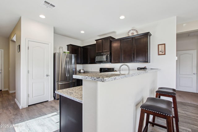 kitchen with stainless steel fridge, a kitchen breakfast bar, light stone counters, dark brown cabinets, and light hardwood / wood-style flooring