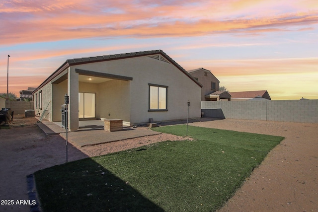 back house at dusk featuring a patio and a lawn