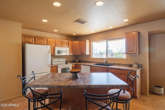 kitchen featuring white appliances, light tile patterned floors, visible vents, a breakfast bar area, and a sink