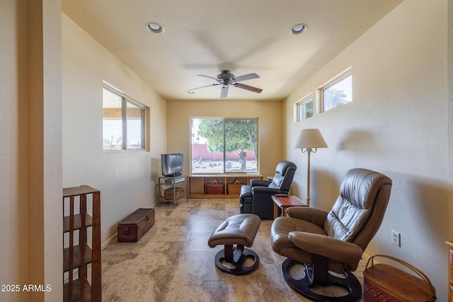 living area with ceiling fan and baseboards