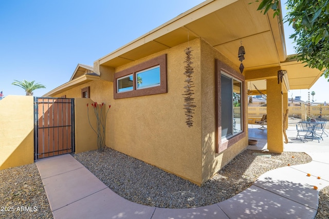 view of side of property featuring a gate, a patio area, fence, and stucco siding