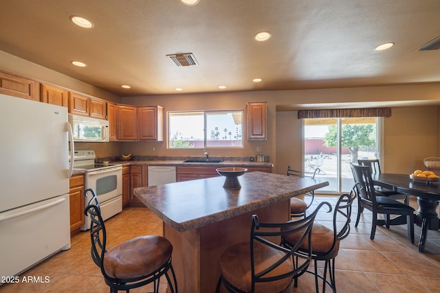 kitchen with white appliances, a kitchen bar, a sink, and visible vents