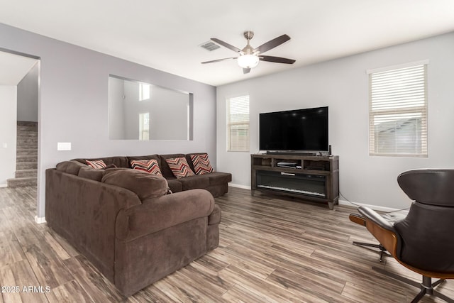 living room with stairs, wood finished floors, visible vents, and a ceiling fan