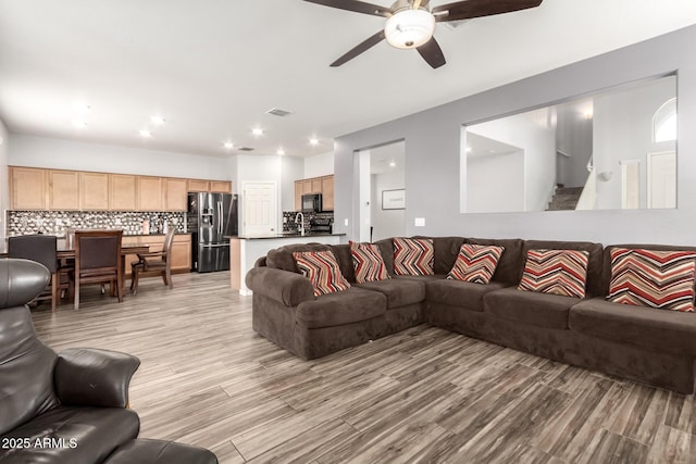 living room featuring visible vents, light wood-style flooring, stairs, and a ceiling fan