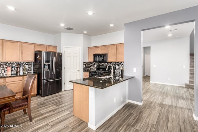 kitchen featuring visible vents, black appliances, light wood-style flooring, dark stone countertops, and a peninsula