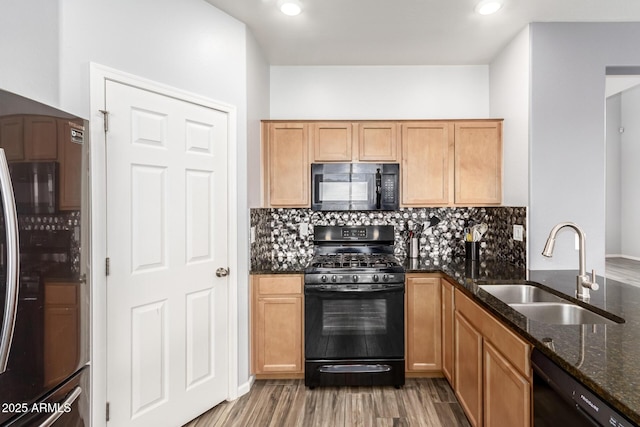 kitchen with a sink, decorative backsplash, black appliances, and dark stone counters