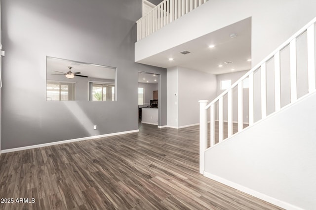 unfurnished living room featuring stairway, wood finished floors, visible vents, baseboards, and a towering ceiling