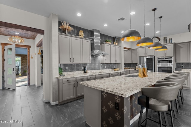 kitchen with wall chimney exhaust hood, gray cabinets, a sink, and stainless steel appliances