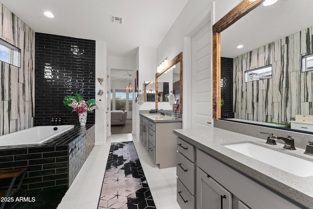 bathroom featuring tiled bath, two vanities, a sink, visible vents, and tile patterned floors