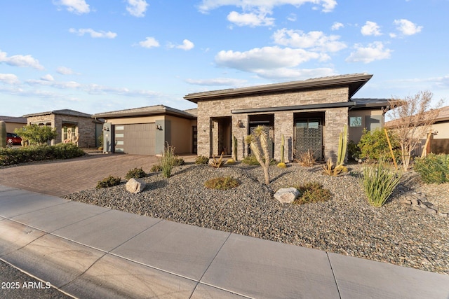 prairie-style home featuring an attached garage, stone siding, decorative driveway, and stucco siding