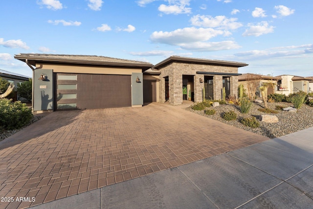 prairie-style home with stone siding, decorative driveway, an attached garage, and stucco siding