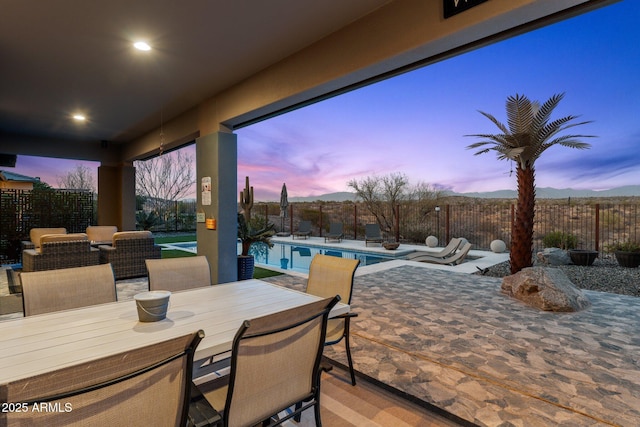 patio terrace at dusk featuring outdoor dining space, a fenced backyard, and a fenced in pool