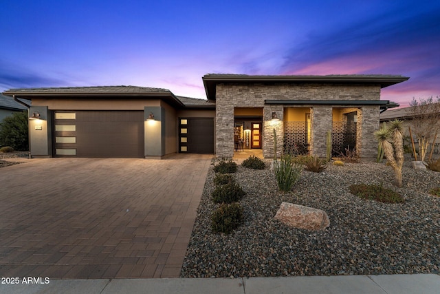 prairie-style home with a garage, stone siding, decorative driveway, and stucco siding