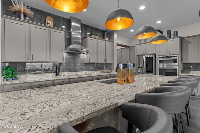 kitchen featuring wall chimney range hood, gray cabinets, stainless steel appliances, and a sink