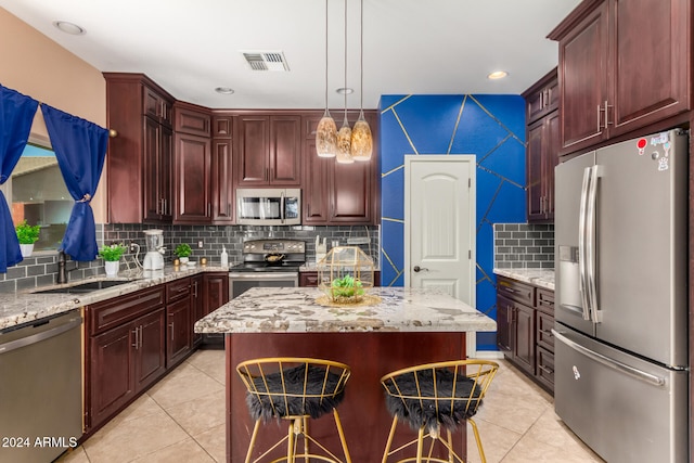 kitchen featuring decorative backsplash, light tile patterned floors, decorative light fixtures, a kitchen island, and stainless steel appliances