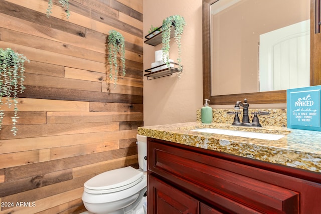 bathroom with vanity, toilet, and wooden walls