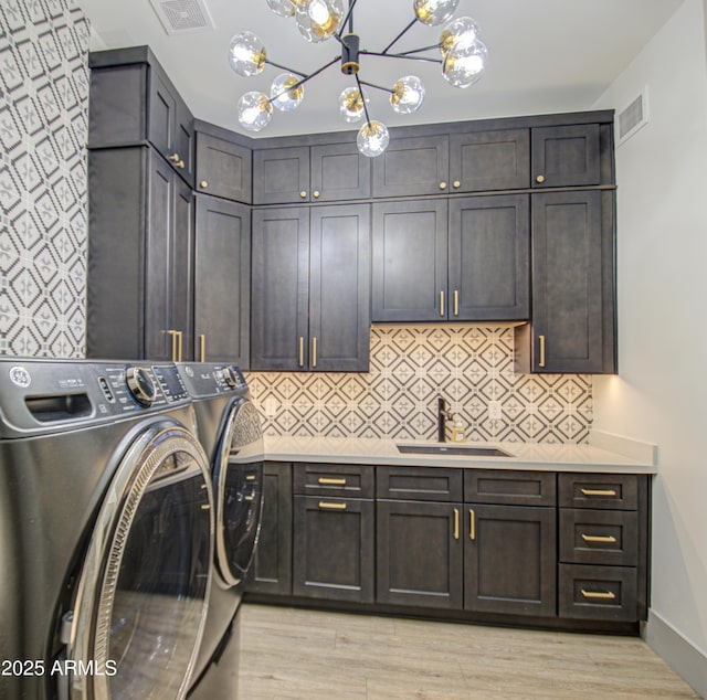 laundry room with sink, cabinets, washer and dryer, a notable chandelier, and light hardwood / wood-style floors