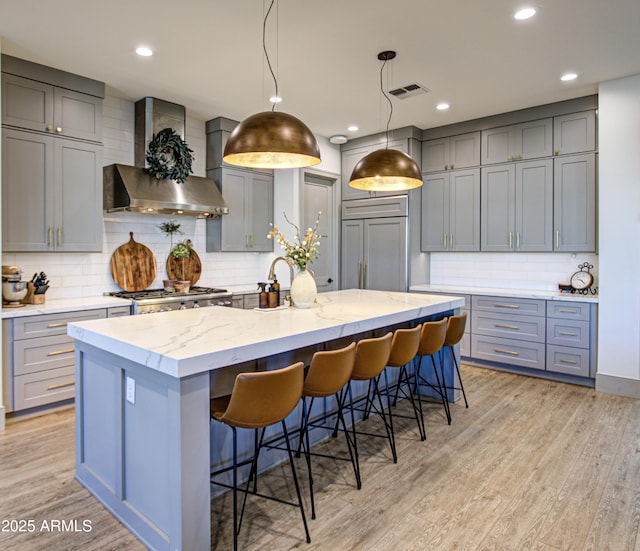 kitchen featuring pendant lighting, a breakfast bar, a spacious island, light hardwood / wood-style floors, and wall chimney exhaust hood