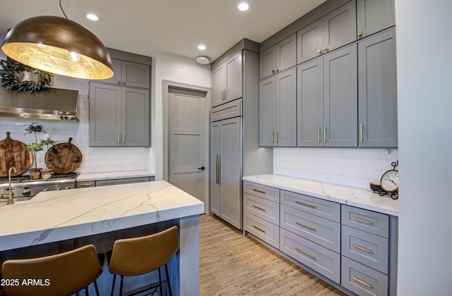 kitchen featuring light stone counters, gray cabinets, light hardwood / wood-style floors, and stainless steel gas stovetop