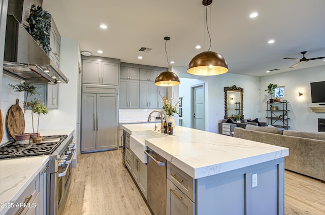 kitchen featuring sink, hanging light fixtures, high end appliances, a kitchen island with sink, and wall chimney range hood