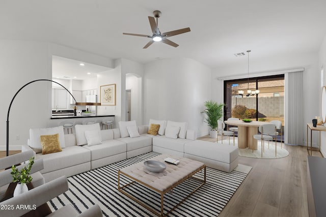 living room with ceiling fan with notable chandelier and light hardwood / wood-style flooring