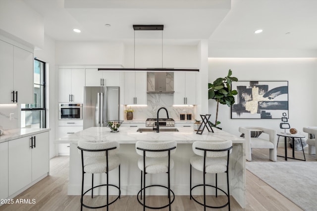 kitchen featuring pendant lighting, appliances with stainless steel finishes, white cabinetry, light stone counters, and a center island with sink