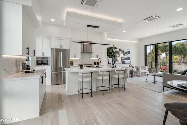 kitchen featuring appliances with stainless steel finishes, light hardwood / wood-style floors, white cabinets, a center island with sink, and decorative light fixtures