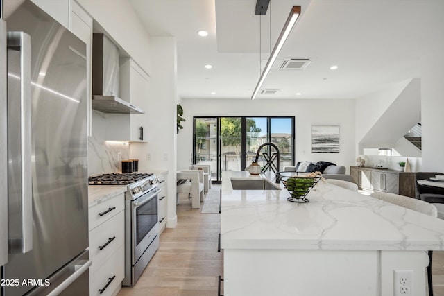 kitchen featuring stainless steel appliances, white cabinetry, hanging light fixtures, and wall chimney exhaust hood