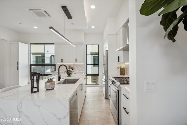 kitchen with sink, stainless steel appliances, wall chimney exhaust hood, and white cabinets