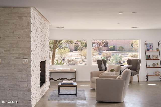 living area featuring concrete flooring and a stone fireplace