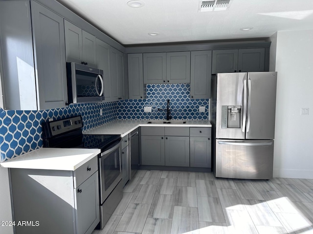 kitchen with sink, tasteful backsplash, gray cabinetry, and stainless steel appliances