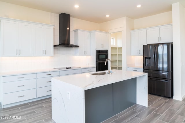 kitchen with white cabinetry, sink, wall chimney exhaust hood, an island with sink, and black appliances