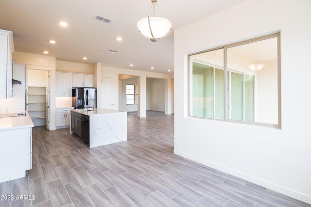 kitchen with decorative light fixtures, white cabinets, stainless steel fridge with ice dispenser, black dishwasher, and an island with sink