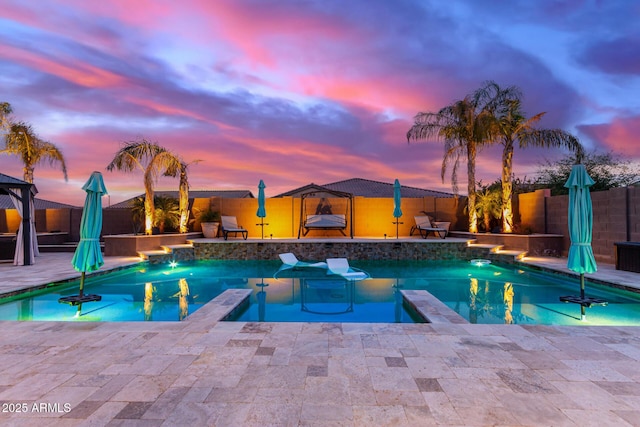 pool at dusk with pool water feature and a patio area