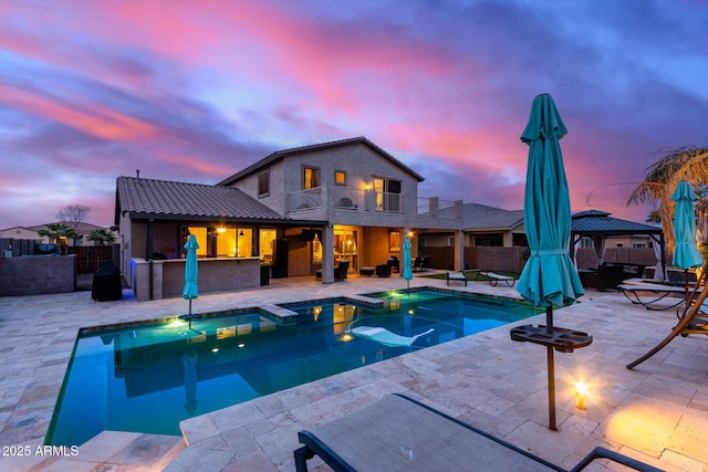 pool at dusk with a gazebo, exterior bar, and a patio area