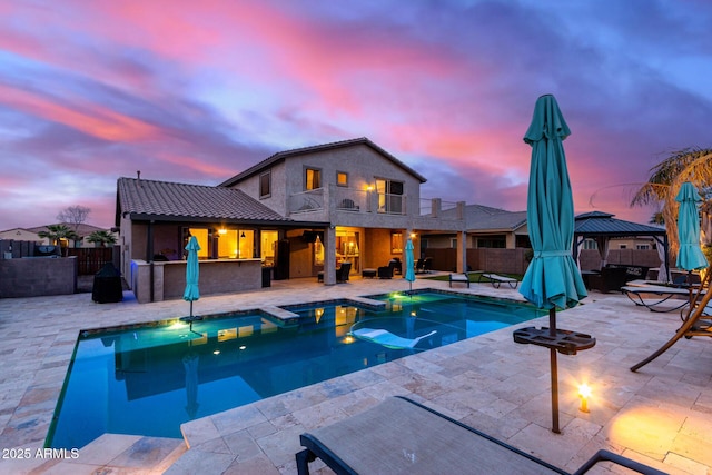 pool at dusk featuring a gazebo, exterior bar, and a patio