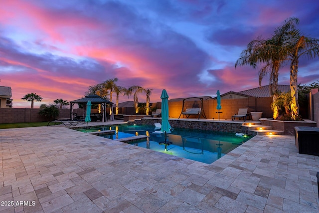 pool at dusk featuring a gazebo, a patio area, pool water feature, and an in ground hot tub