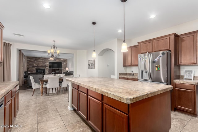 kitchen with a stone fireplace, stainless steel appliances, a center island, light tile patterned flooring, and decorative light fixtures