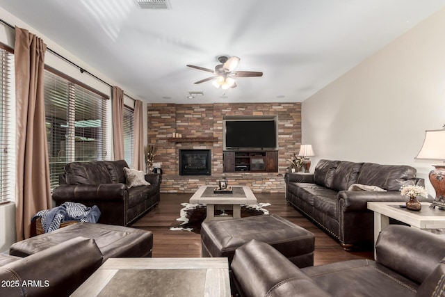 living room featuring dark hardwood / wood-style flooring, a stone fireplace, and ceiling fan