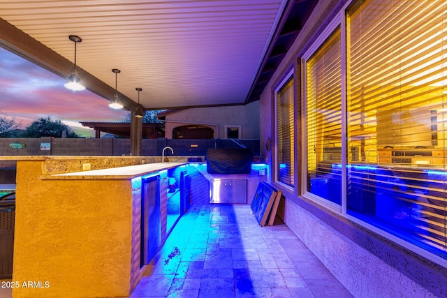 patio terrace at dusk featuring sink, grilling area, and a fenced in pool